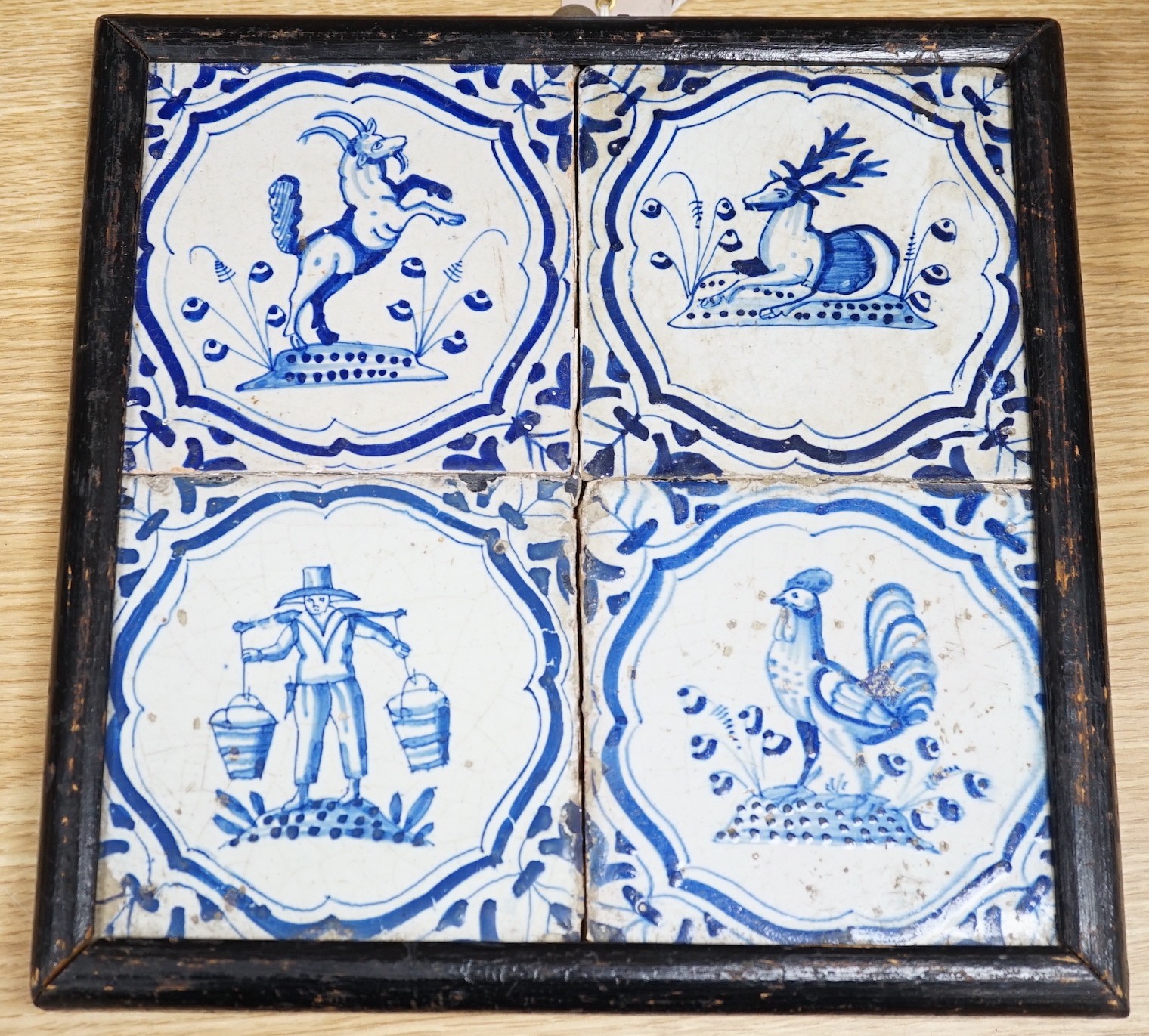 Four 17th century Dutch Delft blue and white tiles, decorated with deer, cockerels and figures within shaped panels (frame 29cm)